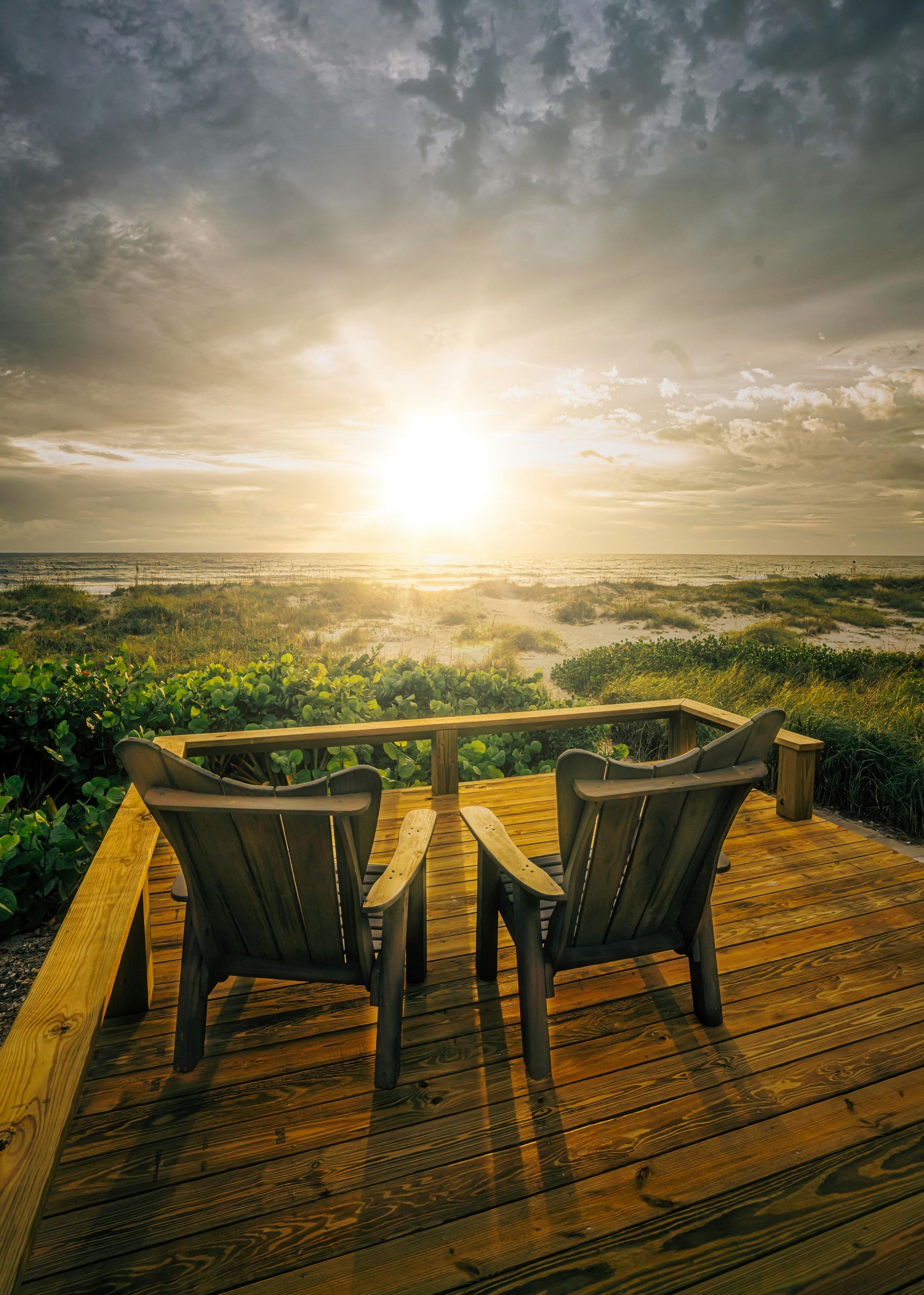 A modern house with dark wood siding and large windows, featuring an outdoor deck area with horizontal railing.