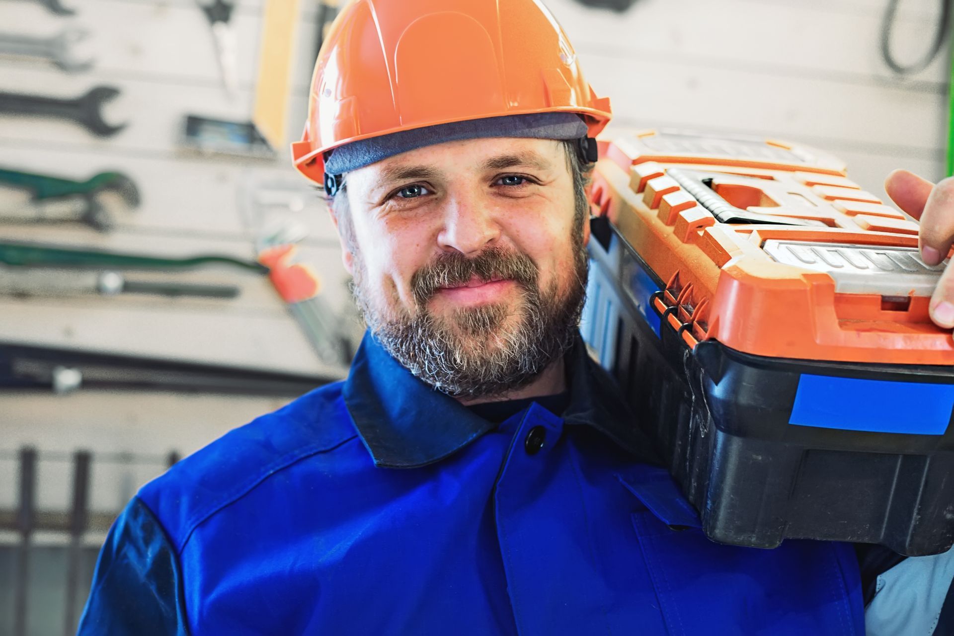 A man wearing a hard hat is carrying a toolbox on his shoulder.