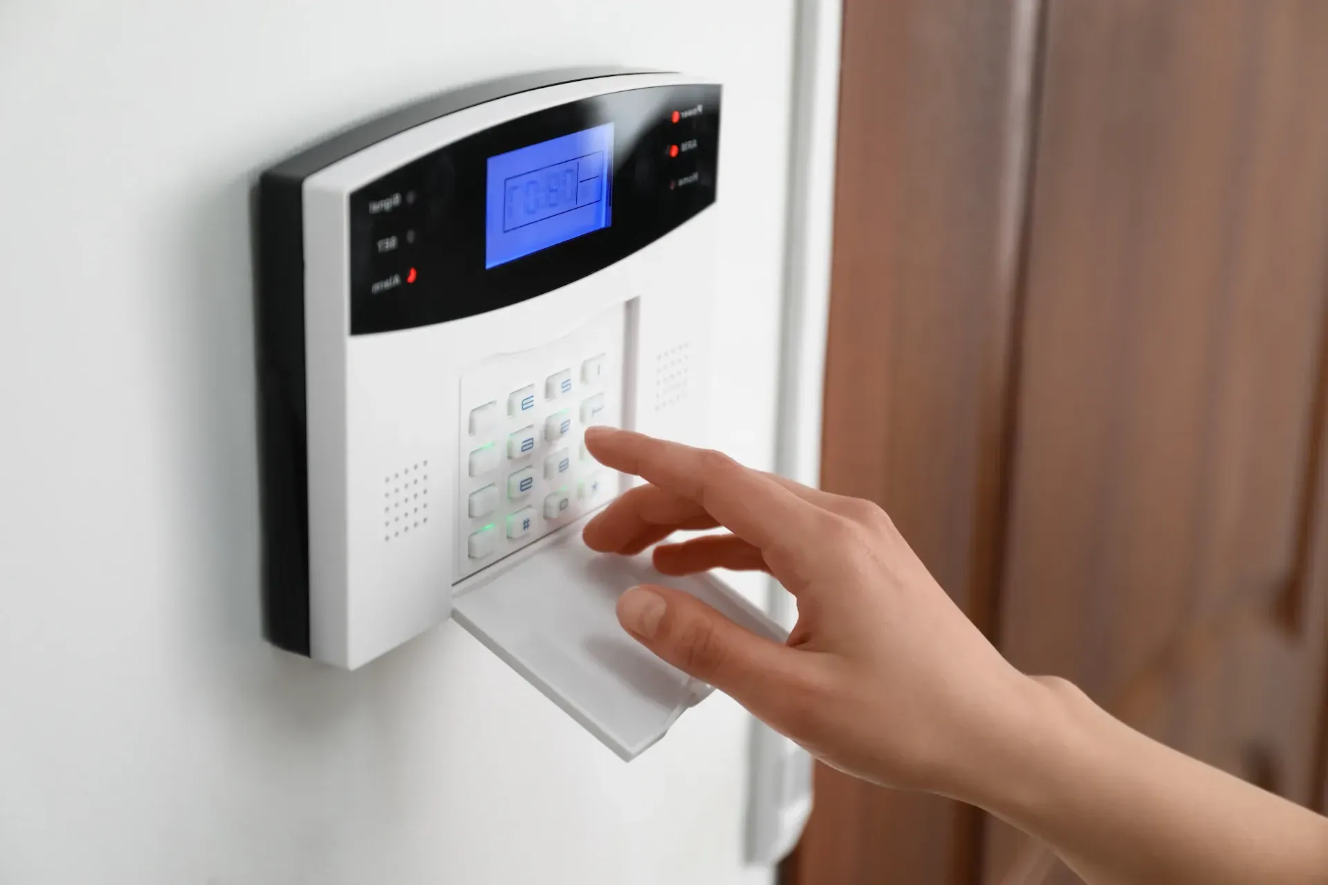 A person's hand entering a PIN code on the digital keypad of a wireless door lock system mounted nex