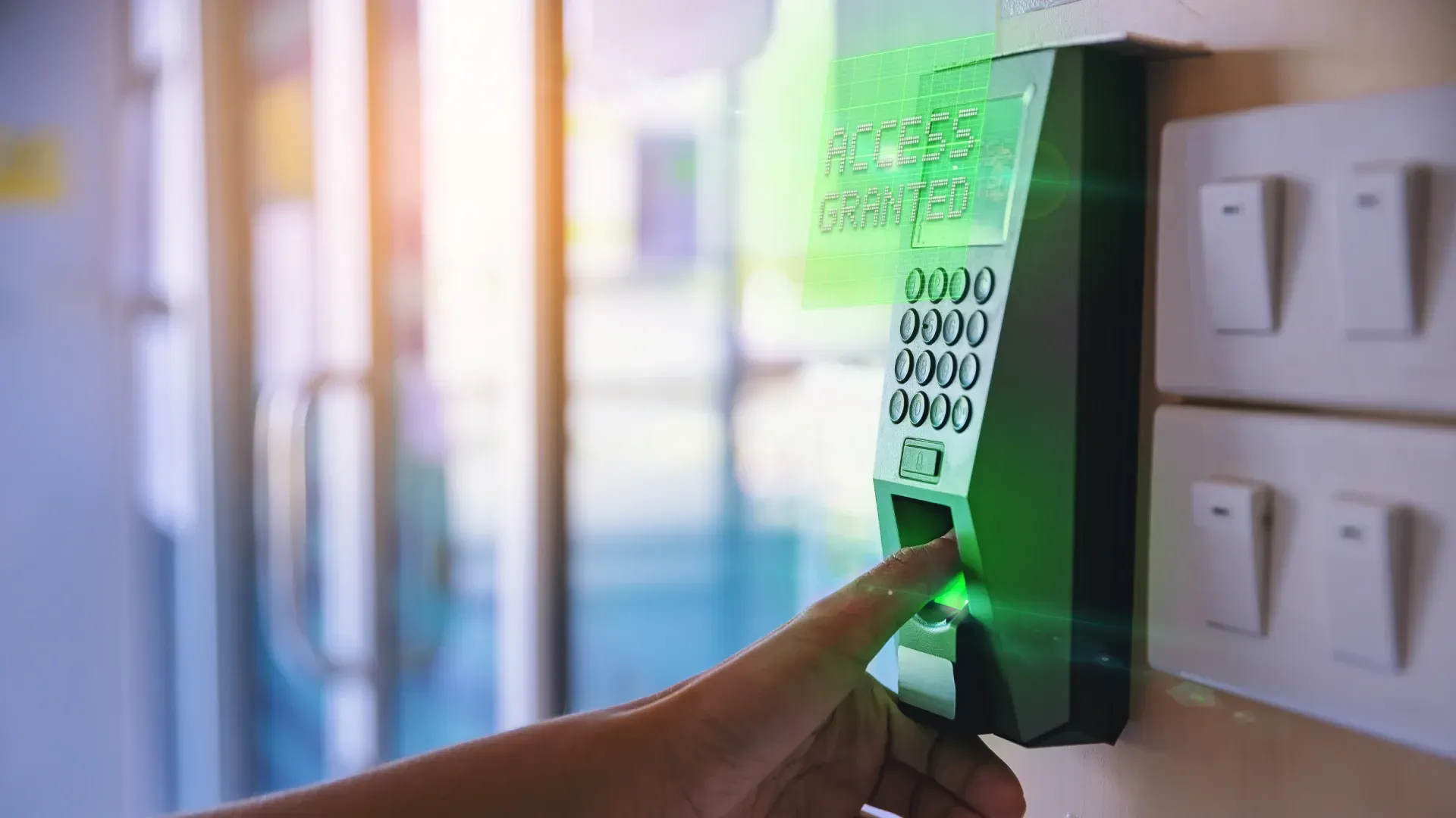 A close-up of a person's finger on a door access system Malaysia fingerprint reader, displaying an '