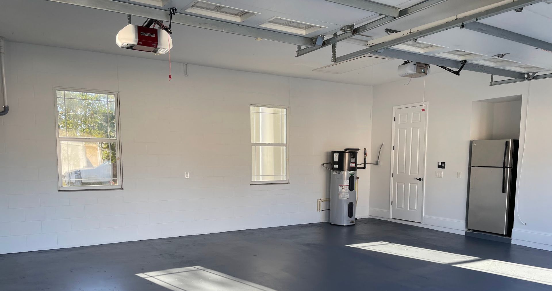 An empty garage with a refrigerator , water heater , and a garage door opener.