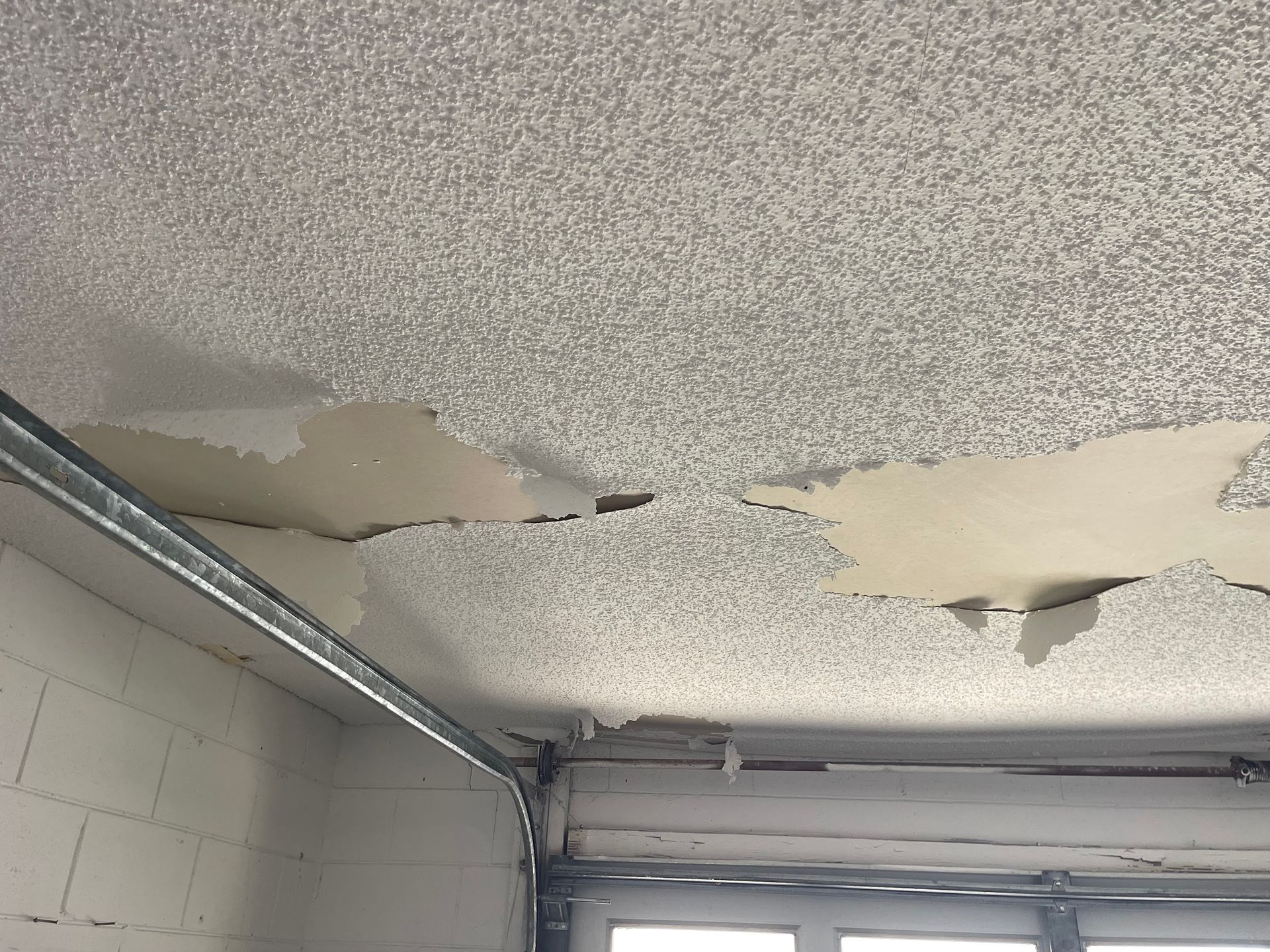 A close up of a ceiling with peeling paint in a garage.