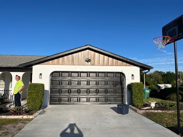 A man is standing in front of a house with a basketball hoop in the driveway.