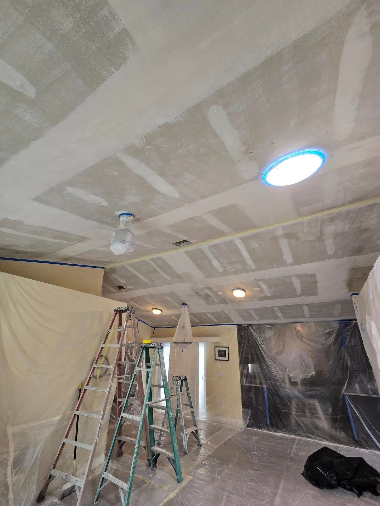 A room with a ceiling that is being painted and a ceiling fan.