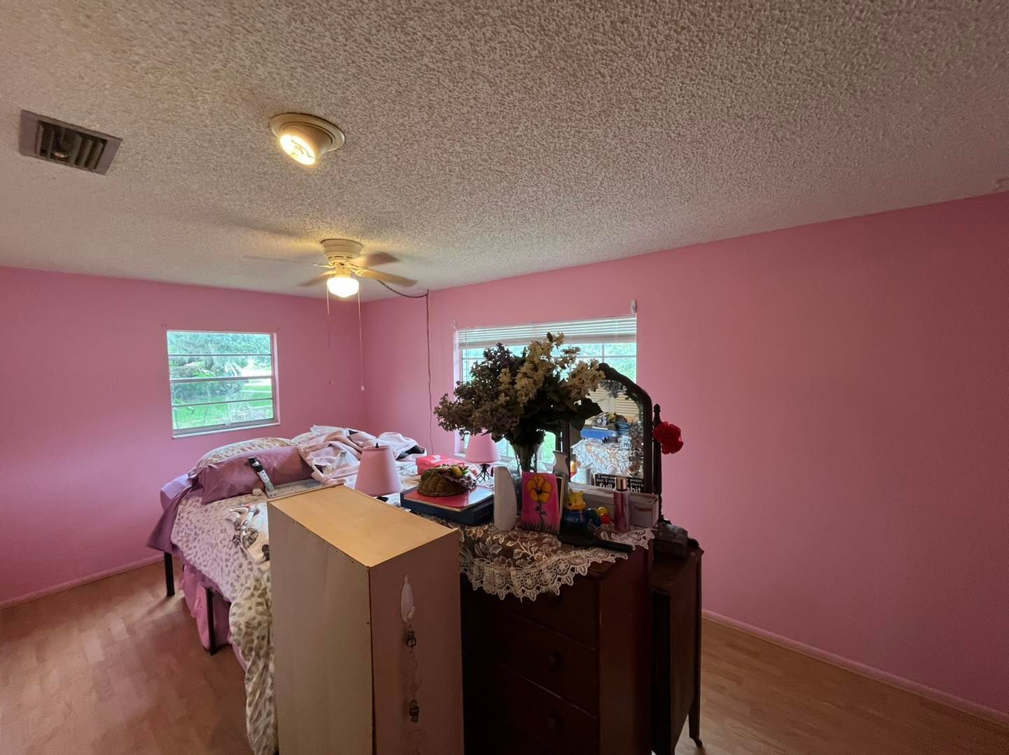 A bedroom with pink walls and a ceiling fan.