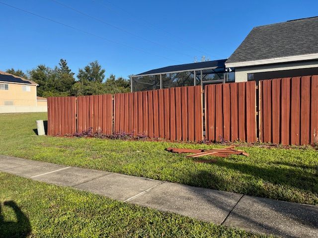 Red wooden fence in a grassy yard, with a sidewalk in front and a house in the background.