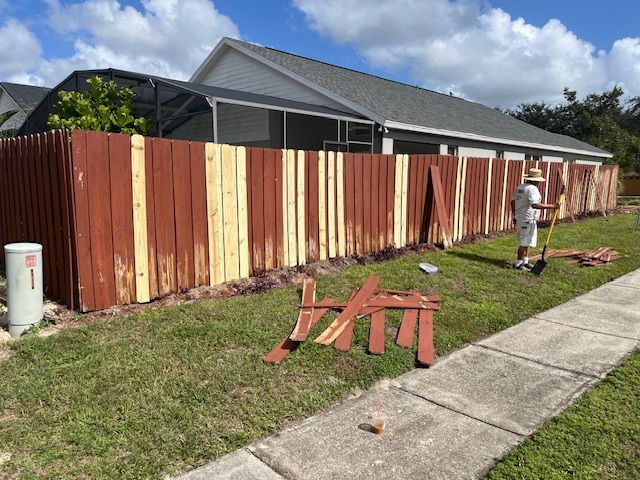 Person painting a wooden fence red and beige outside a house.