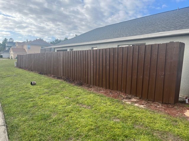 Brown wooden privacy fence along a grassy yard next to a house under a cloudy sky.
