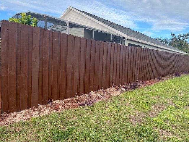 Brown wooden fence bordering a lawn and house with a clear blue sky.