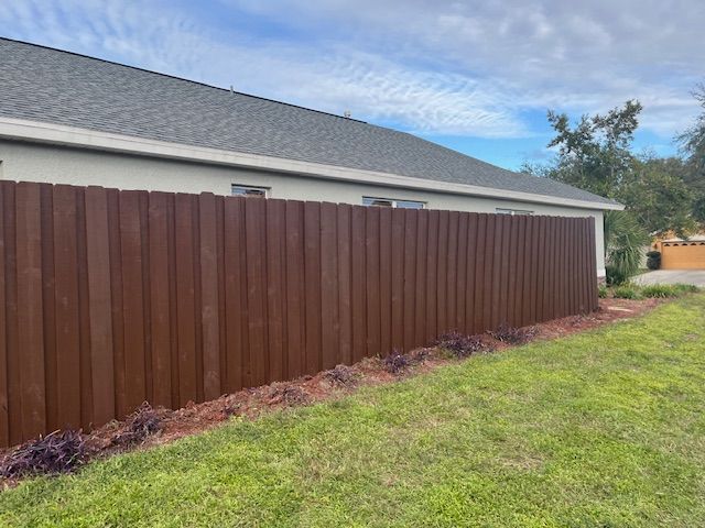 Brown wooden fence along a building, next to green grass and a mulch bed.