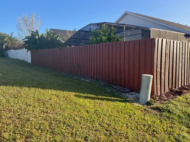 Red and white fences border a grassy lawn. A house and screened-in pool enclosure are visible in the background.
