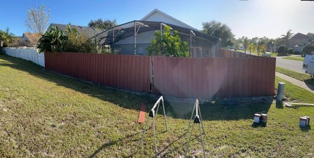 Red fence surrounding a home's backyard with green grass. Paint cans and equipment are in the foreground.