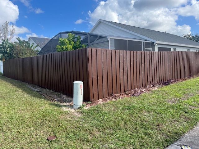 Brown wooden fence surrounding a house with a screen-enclosed pool on a sunny day.