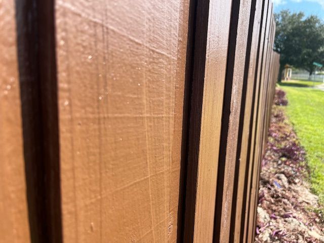 Brown painted wooden fence in a yard with green grass and purple plants.