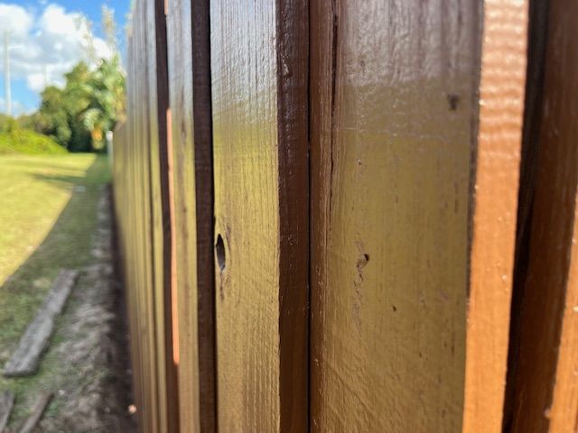 Wooden fence with a brown-toned paint, extending into a green yard under a blue sky.