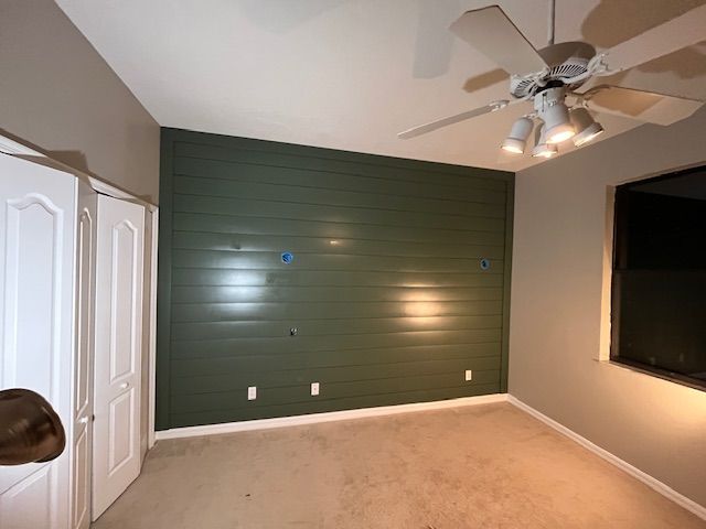 Bedroom with green accent wall, white doors, tan carpet, and ceiling fan.
