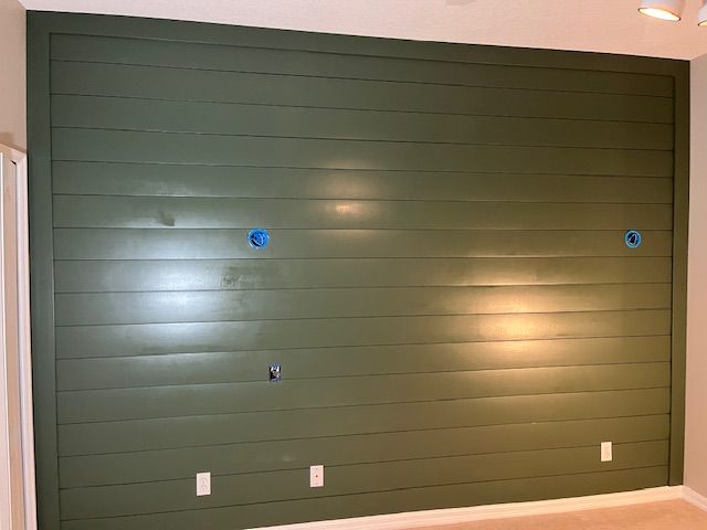 Green shiplap wall with electrical outlets and blue holes.