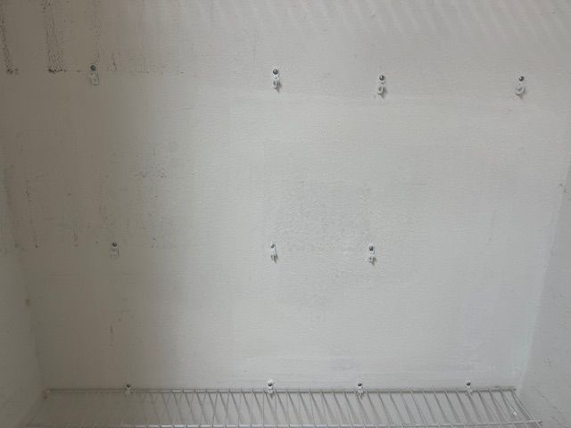 White closet wall with metal wire shelf at the bottom and multiple screws.