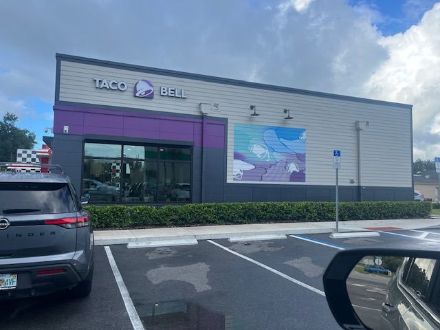 Taco Bell restaurant with purple and grey facade, cloudy sky, and a parking lot.