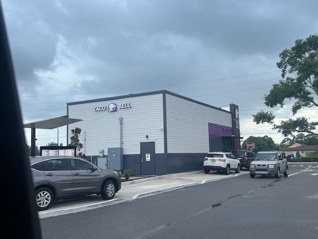 Taco Bell restaurant with cars in the drive-thru lane under a cloudy sky.