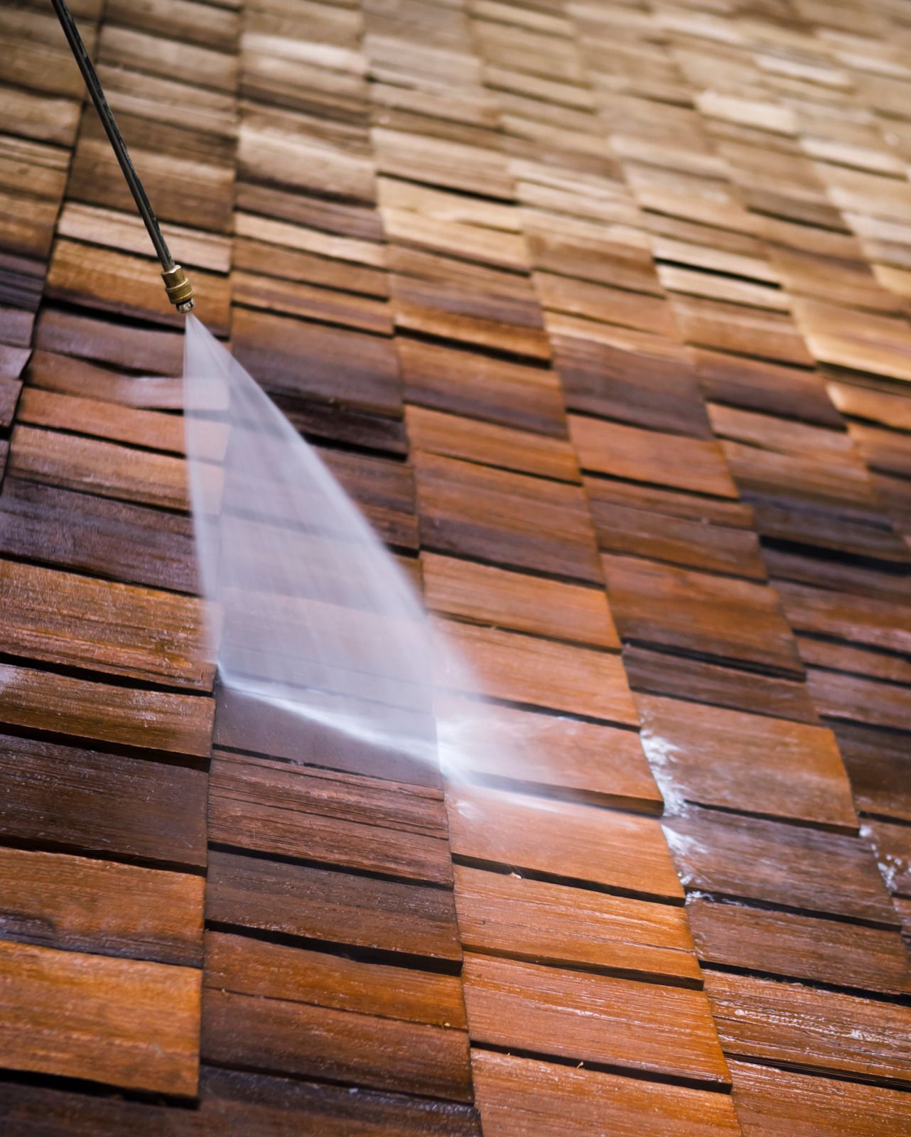 A person is cleaning a wooden roof with a high pressure washer.