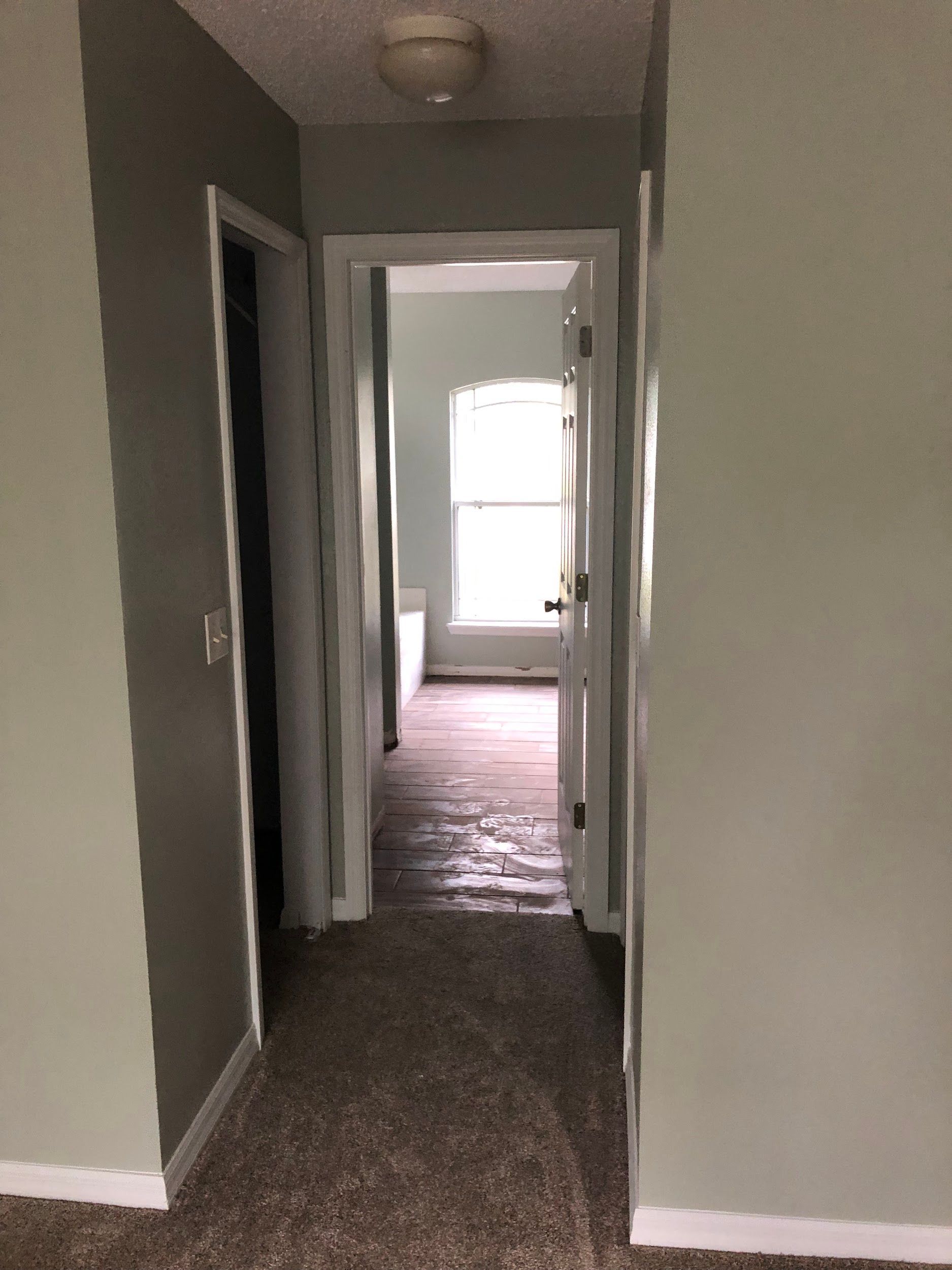 A hallway in a house with a carpeted floor and a window.