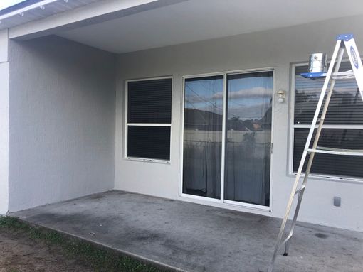 A ladder is sitting on the side of a house next to a sliding glass door.