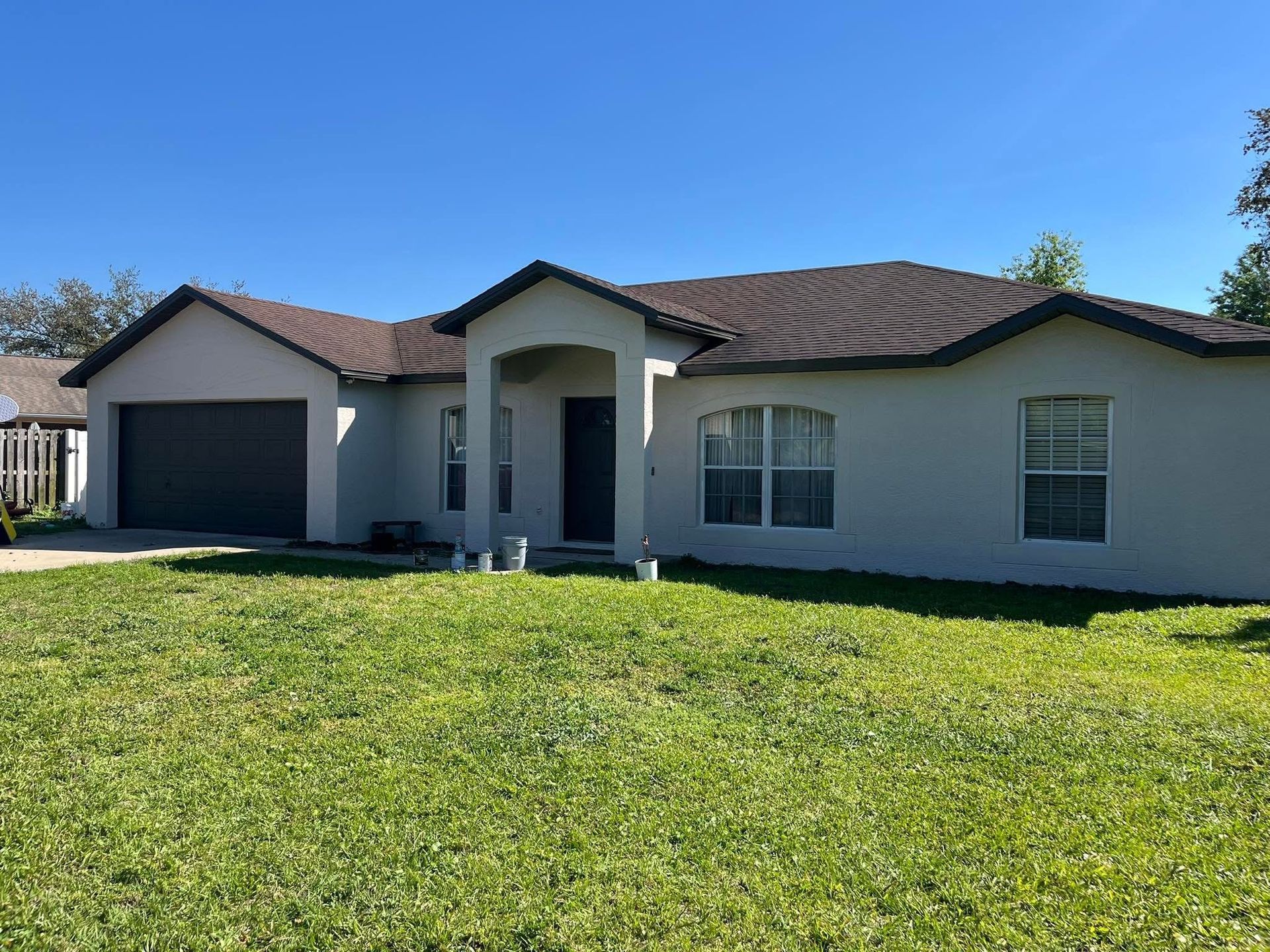 A white house with a brown roof is sitting on top of a lush green lawn.