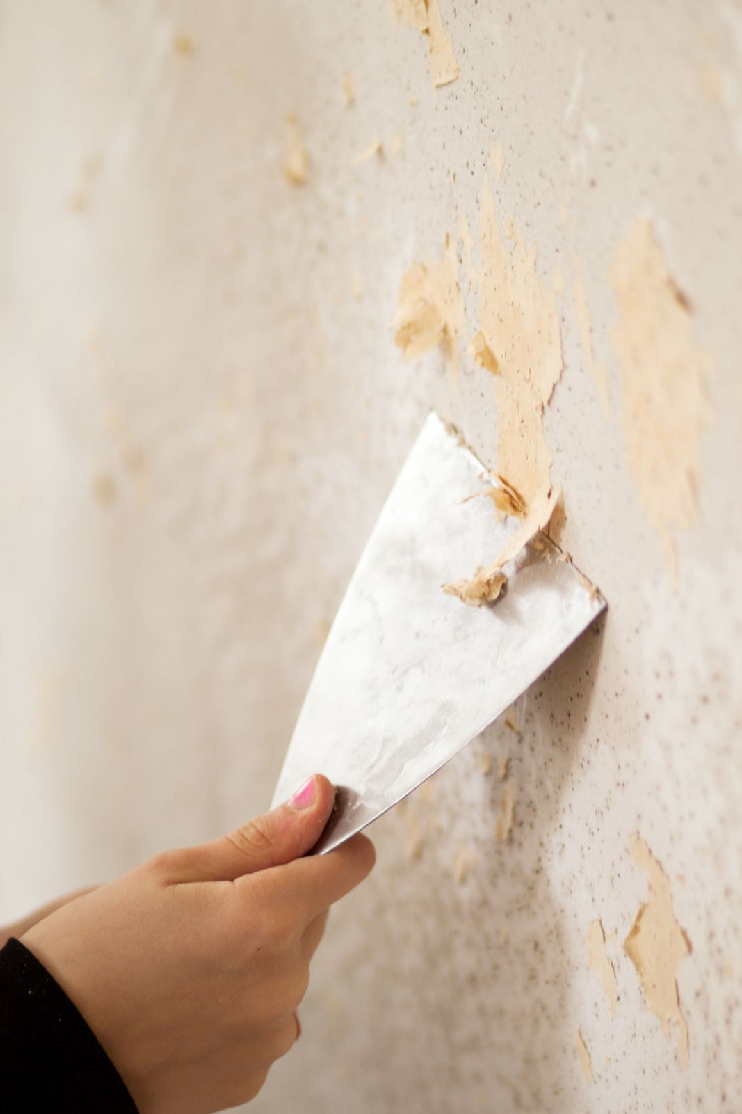 A person is using a spatula to remove wallpaper from a wall.