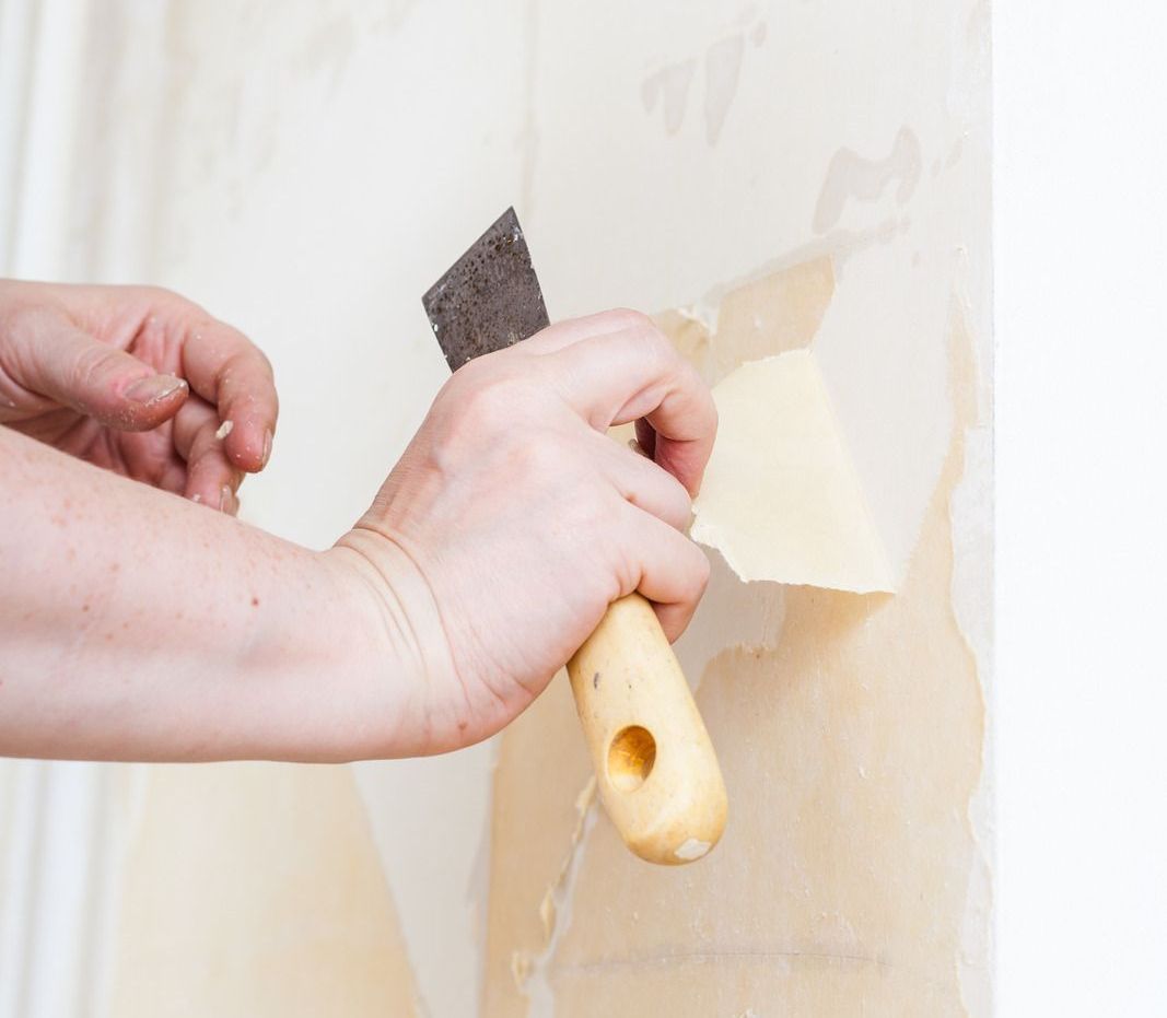 A person is removing wallpaper from a wall with a spatula.