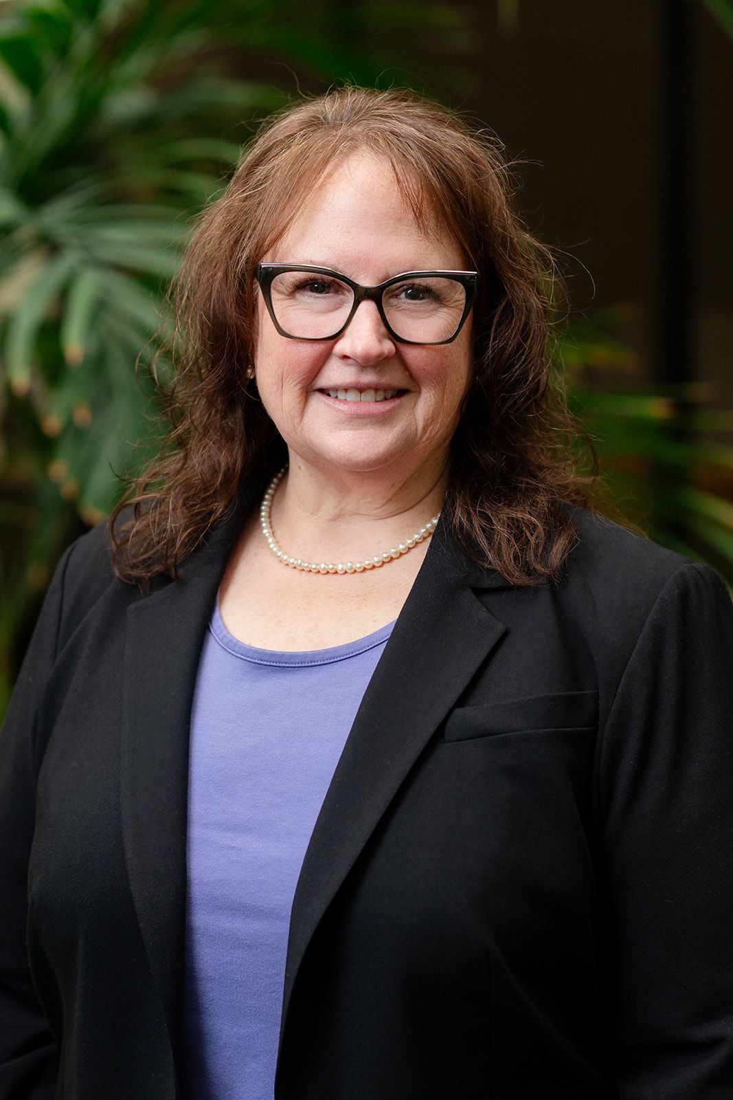 A woman in a blue jacket is standing in front of a bookshelf filled with green books.