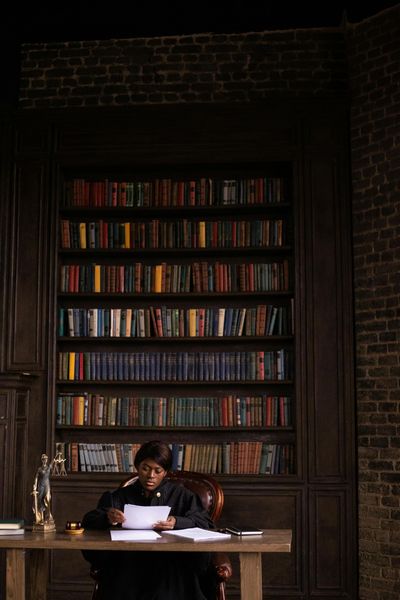 A judge is sitting at a desk in front of a bookshelf.