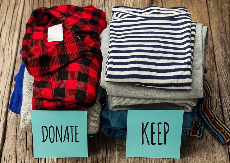 Two stacks of clothes with signs that say donate and keep on a wooden table.