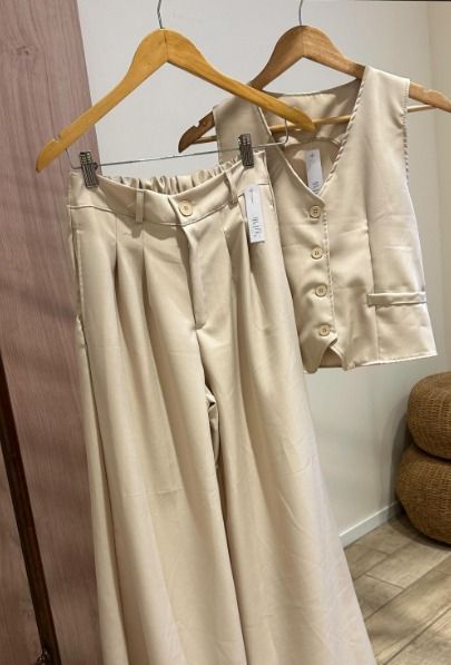 Un par de pantalones beige y un chaleco cuelgan de una percha de madera.