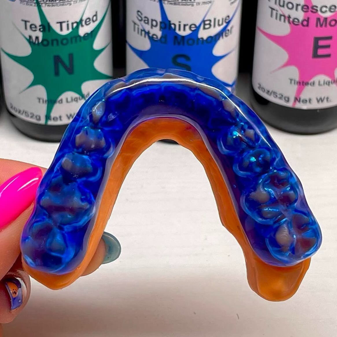 A person with pink nails is holding a blue mouth guard