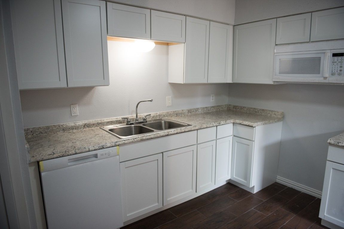 A kitchen with white cabinets , granite counter tops , a sink and a microwave.