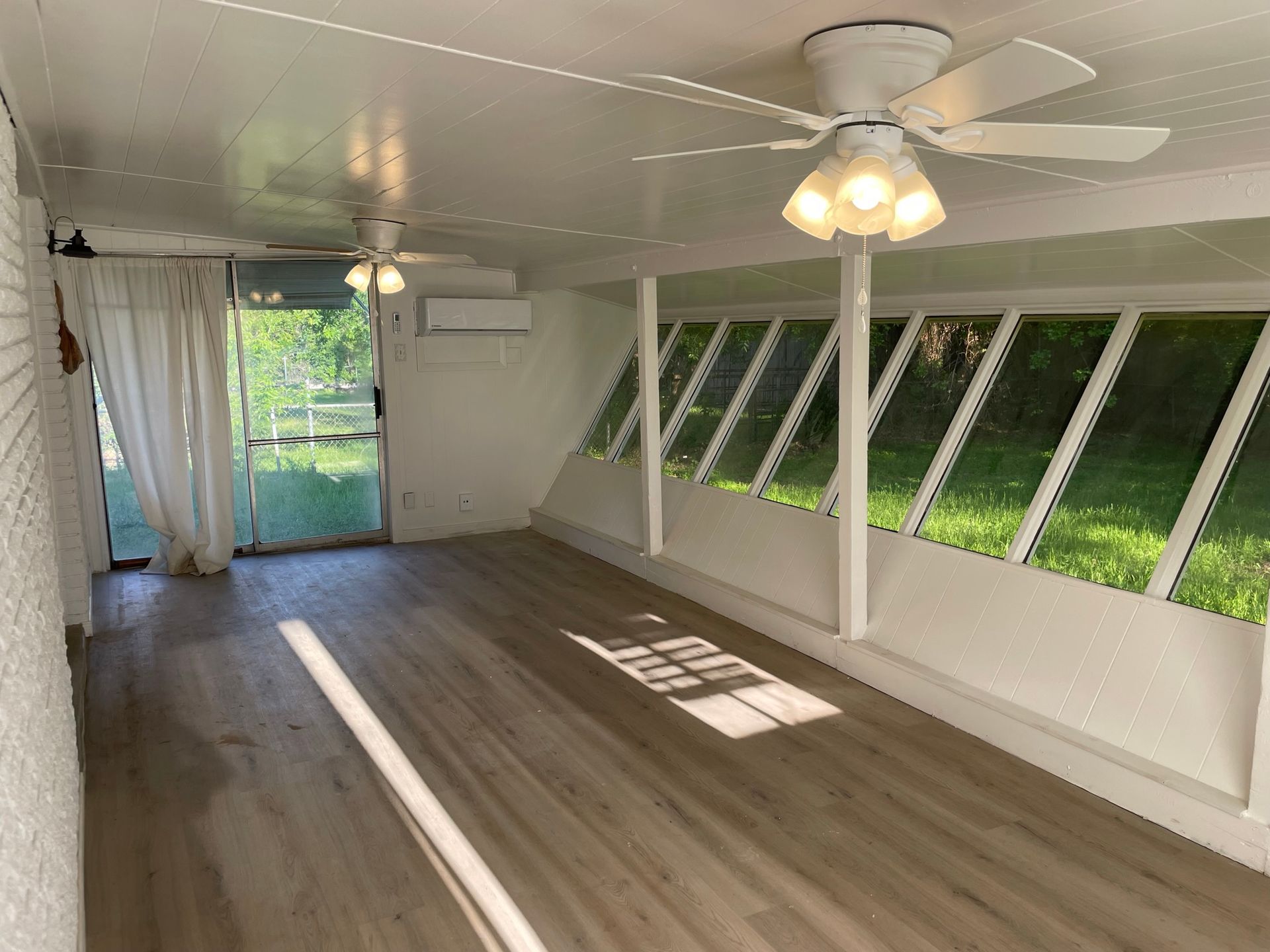 An empty room with a ceiling fan and a lot of windows.