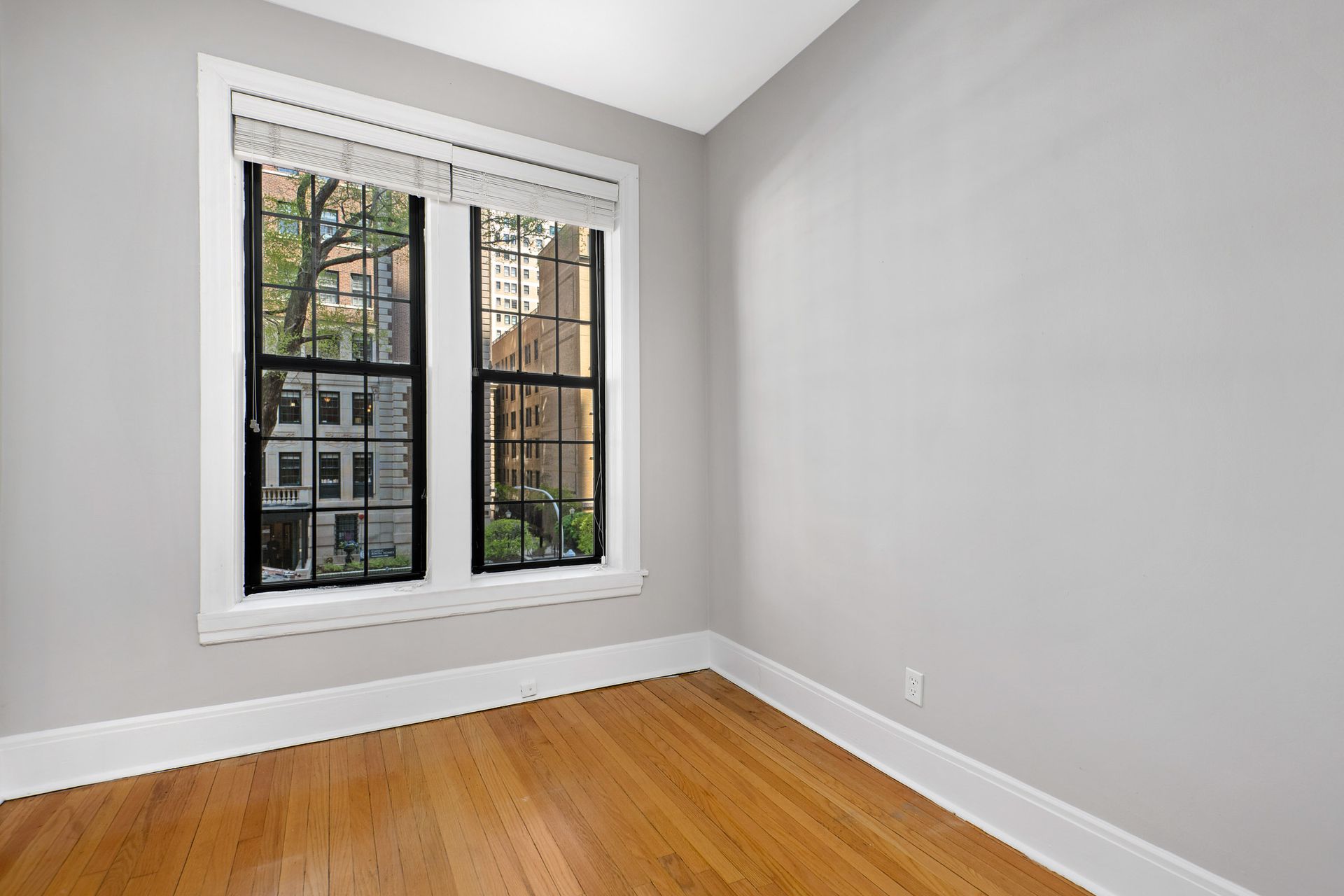 An empty room with two windows and hardwood floors.
