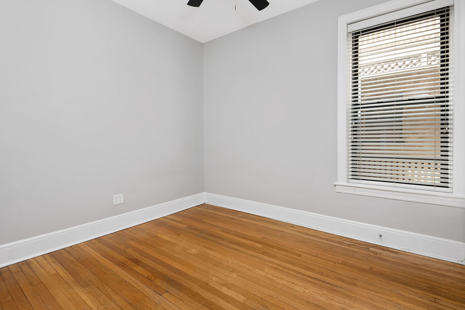 An empty room with hardwood floors and a window with blinds.