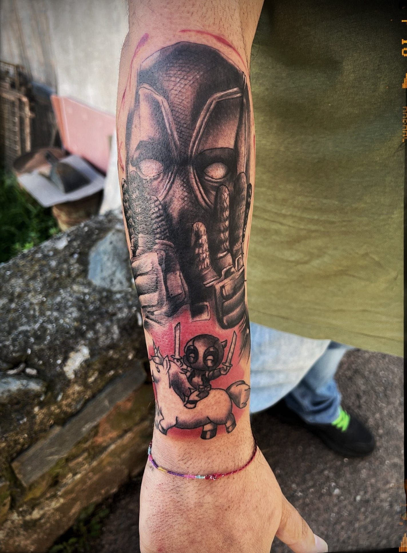 Tatuaggio di una figura con una maschera nera sul braccio, con un teschio e delle ossa sotto. Su sfondo rosso.