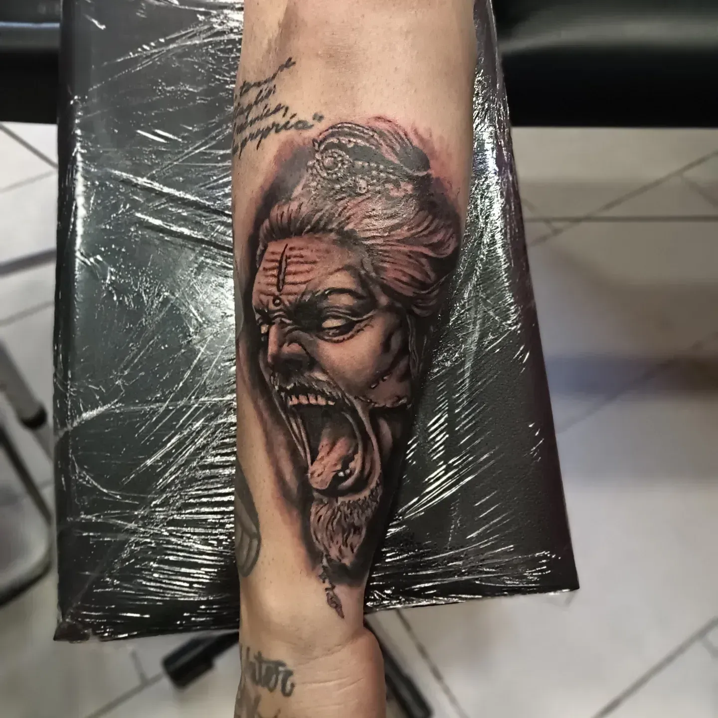 Tatuaggio su un braccio raffigurante un volto urlante nero e grigio, avvolto nella plastica.