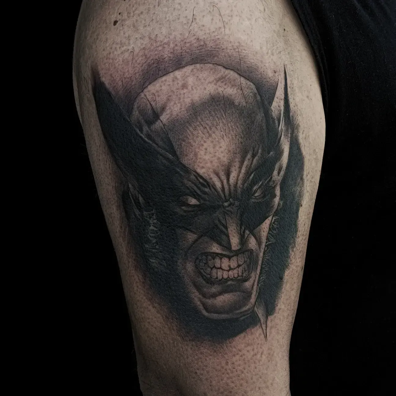 Tatuaggio di Wolverine sulla parte superiore del braccio di una persona. Ritratto in bianco e nero con artigli estesi, ringhianti.