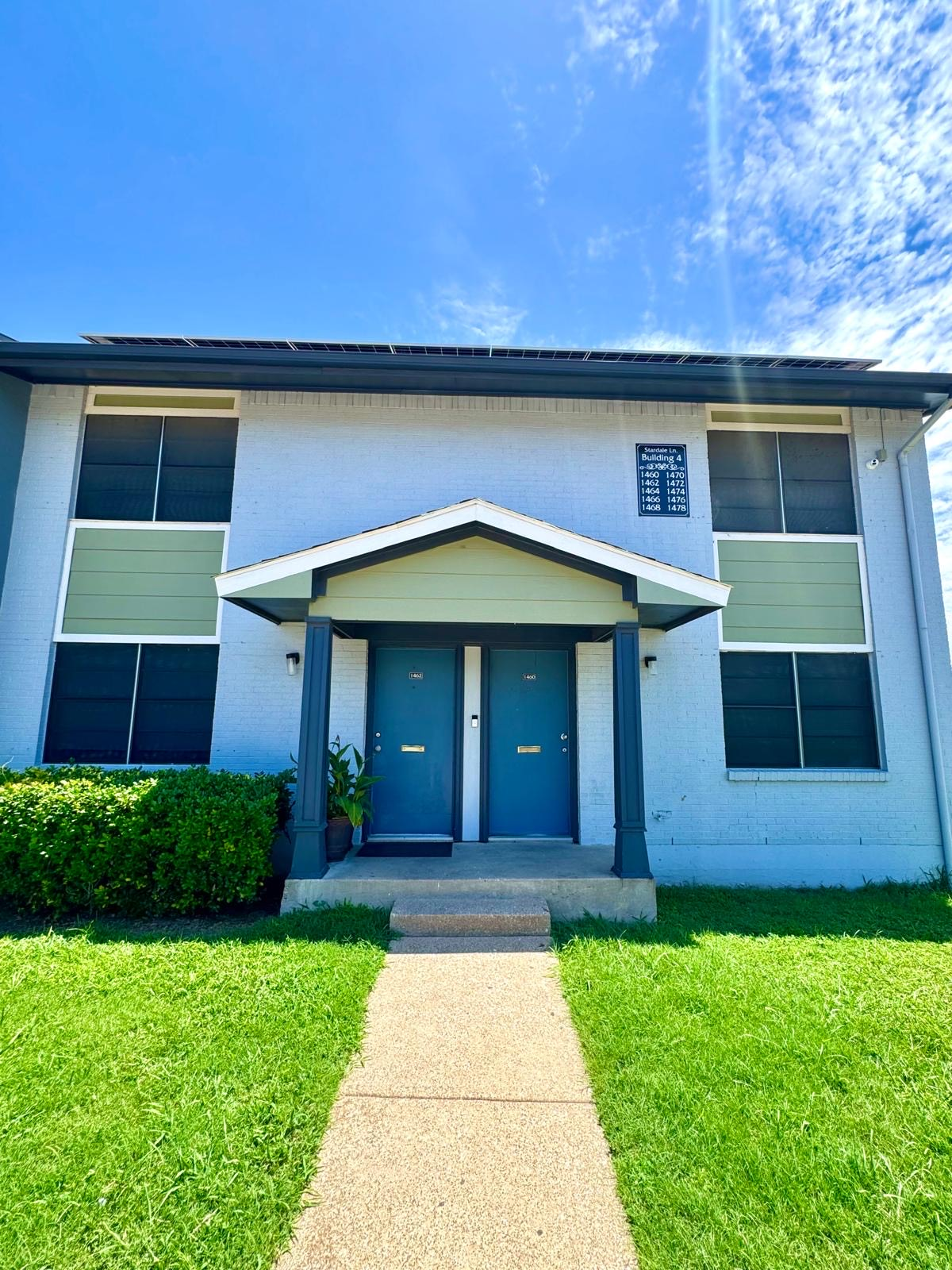 A white apartment building with blue doors and a walkway leading to it.