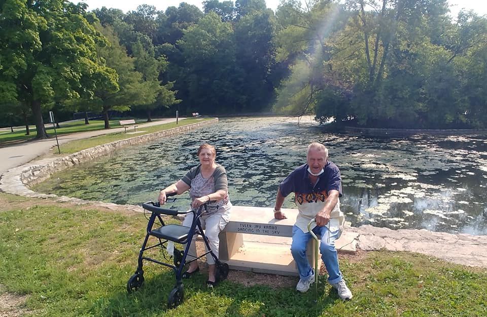 A man and a woman are sitting on a bench in front of a pond.