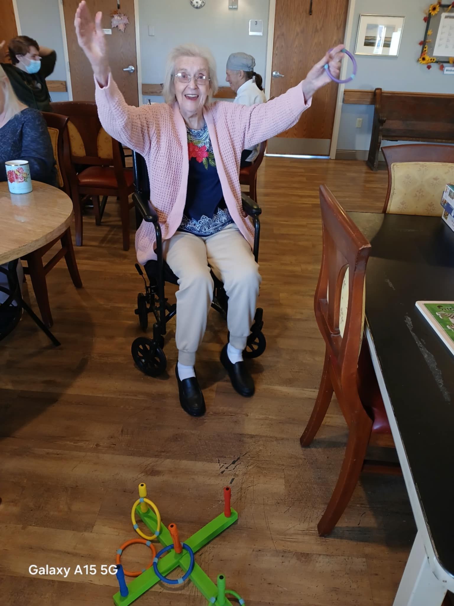 An elderly woman is sitting in a wheelchair with her arms in the air.