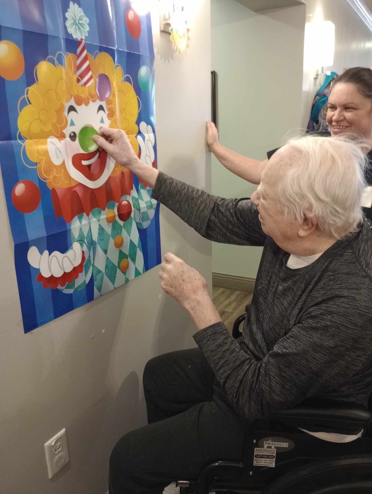 A man in a wheelchair is playing a game with a clown poster on the wall.