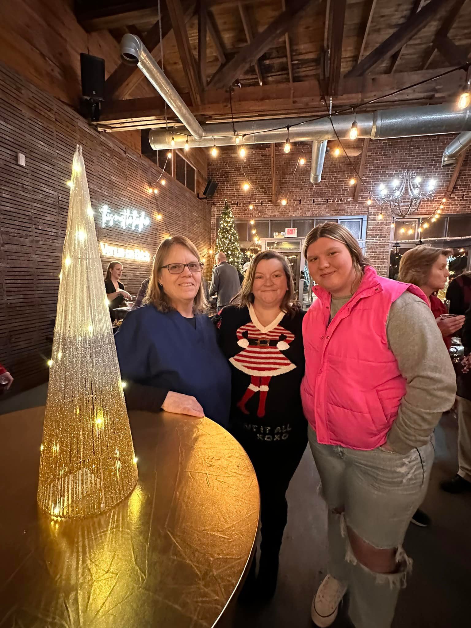 Three women are posing for a picture in a room with a christmas tree in the background.