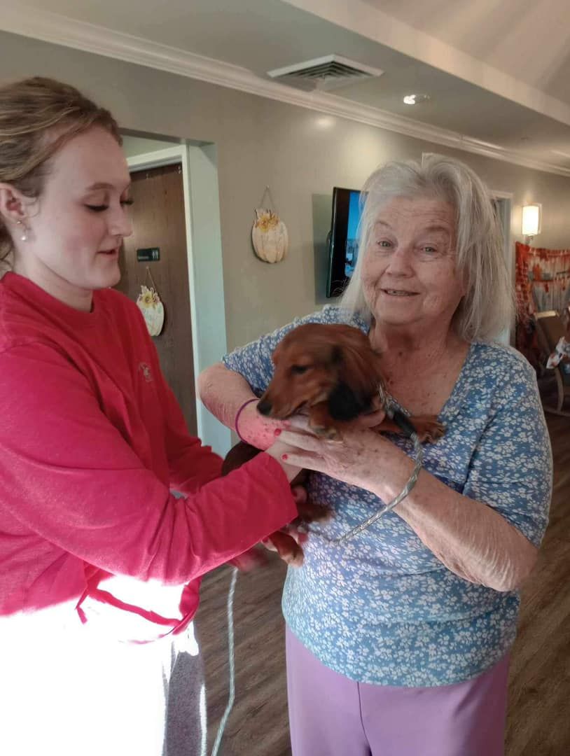 A woman is holding a dog in her arms while another woman looks on.