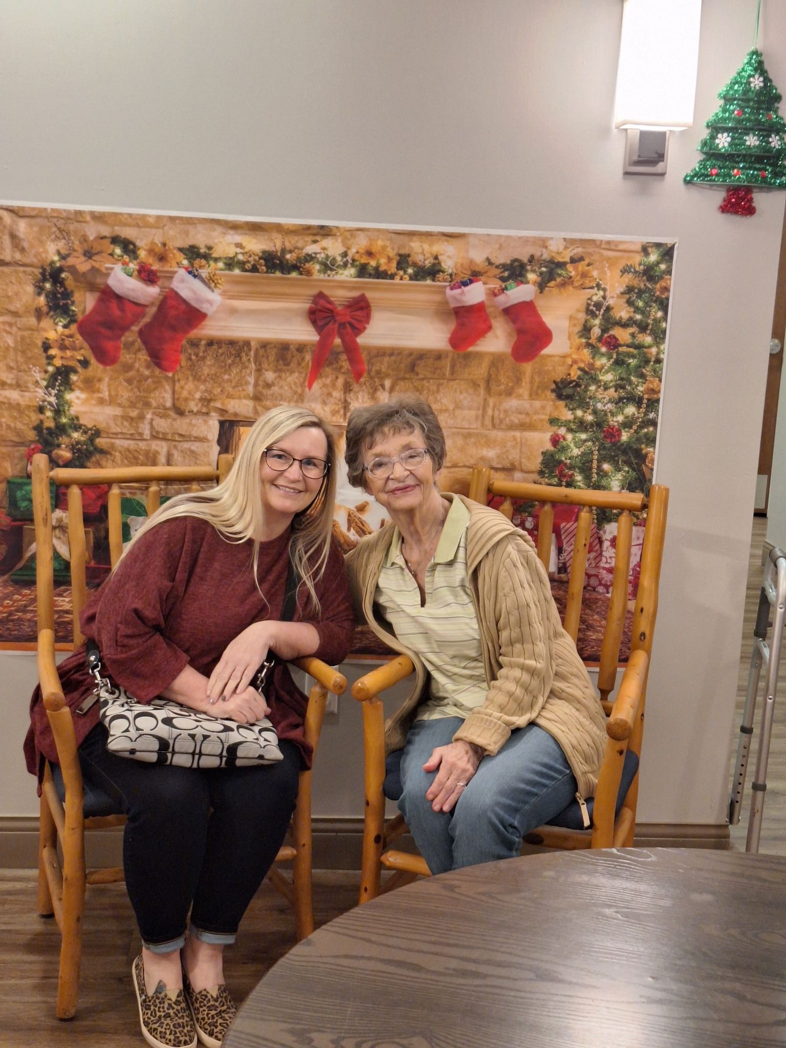 Two women are sitting in chairs in front of a christmas tree.