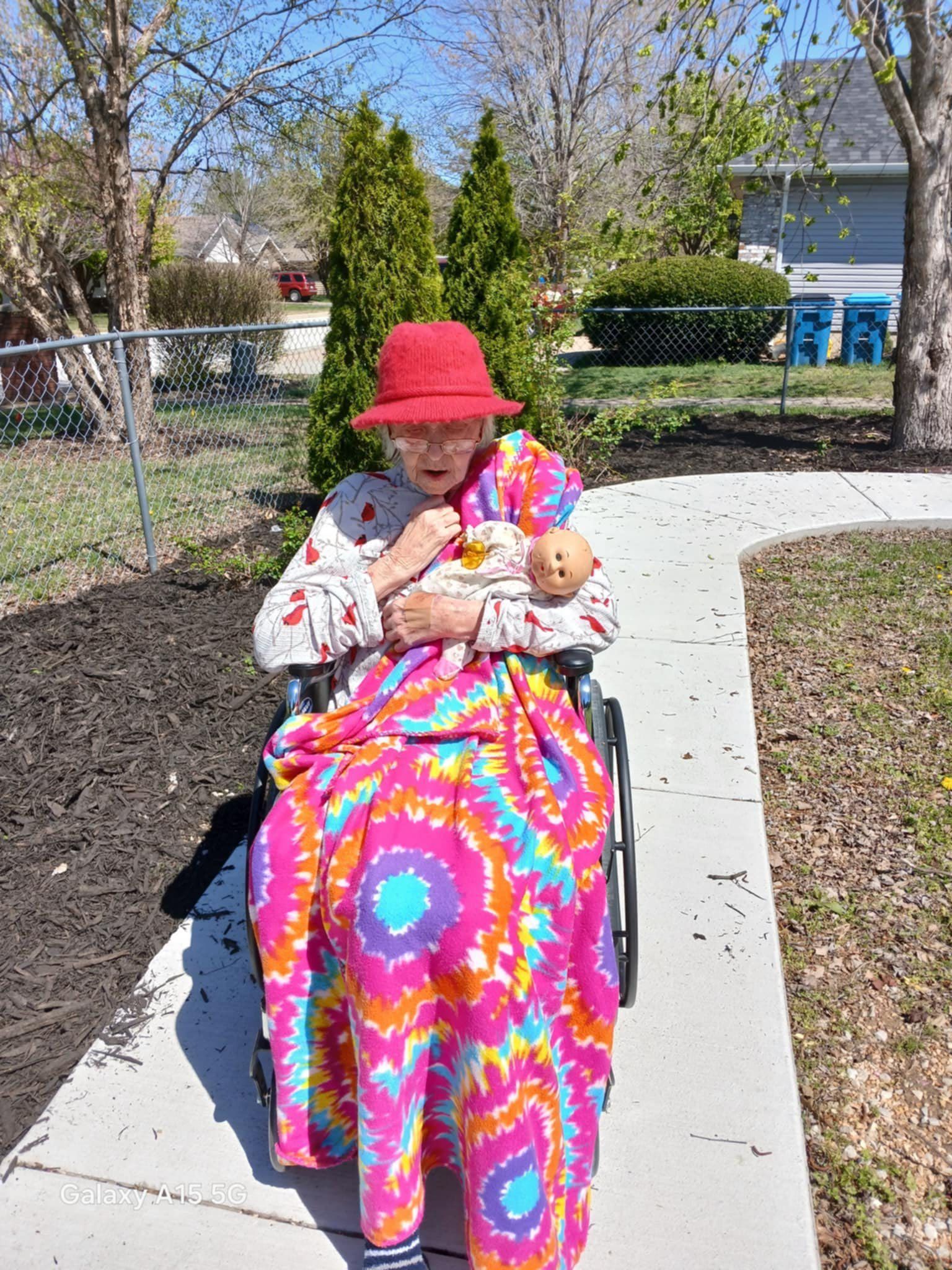 An elderly woman is sitting in a wheelchair holding a doll.